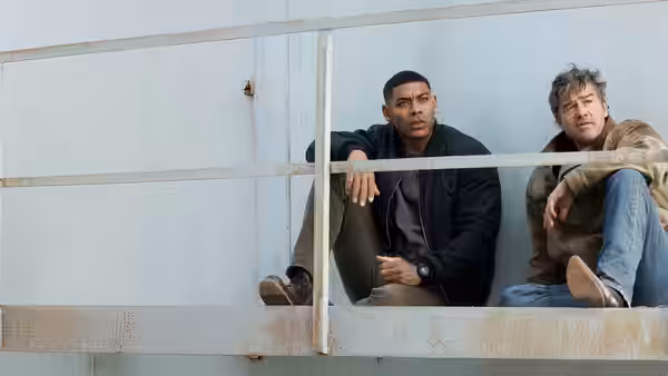 John Stewart (Aaron Pierre) and Hal Jordan (Kyle Chandler) sit side by side on a metal railing