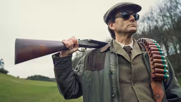 Tony Baddingham (David Tennant) carrying a shotgun over his shoulder outdoors