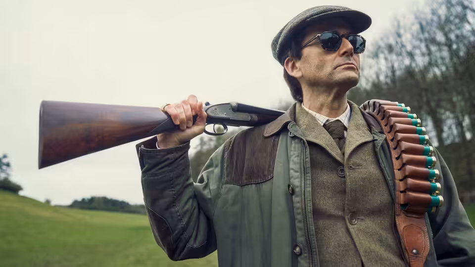 Tony Baddingham (David Tennant) carrying a shotgun over his shoulder outdoors