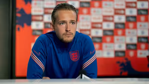 Will Antenbring as Harry Kane seated at a press conference wearing an England tracksuit