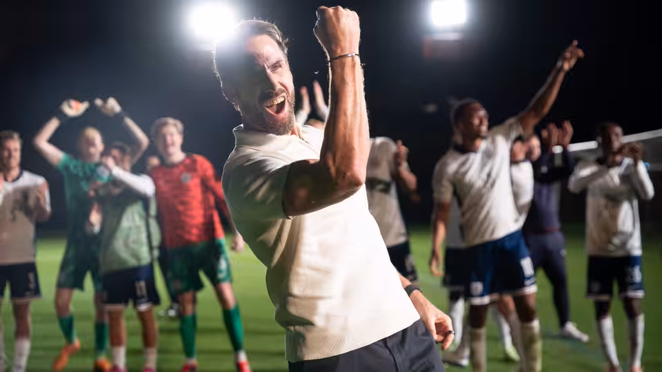 Joseph Fiennes as Gareth Southgate raising his arms in celebration on the pitch