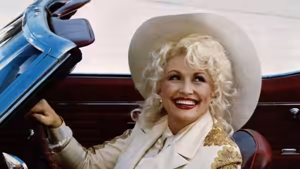 Mona Stangley (Dolly Parton) smiling in the front seat of a convertible car