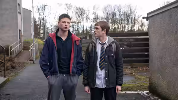 Two young men stand together on a paved outdoor path