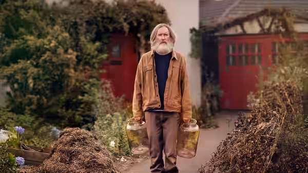 Brian Sleep (Michael Palin) carrying two containers outside a house