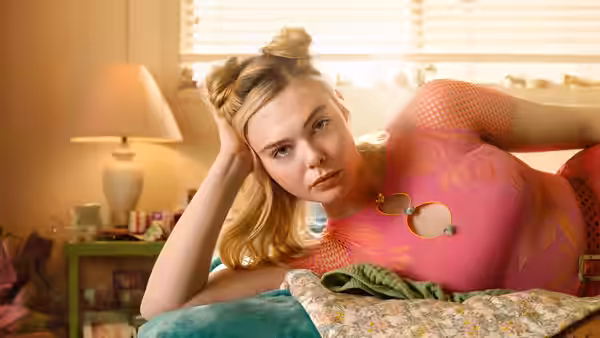 Margo (Elle Fanning) reclines on bed with hand resting on her head
