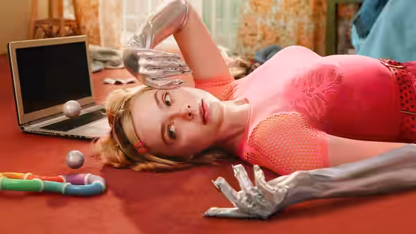 Margo (Elle Fanning) lies on red floor wearing silver gloves near laptop