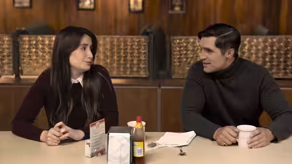 A woman and man talking across a table in a diner booth