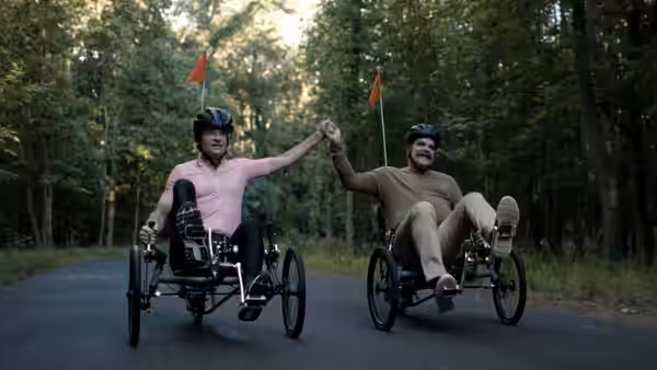 David Harbour and a man in handcycles holding hands on a forest road