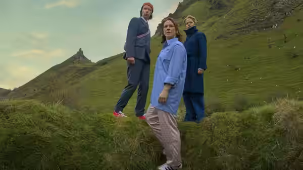 Three people standing on a grassy hillside under an overcast sky