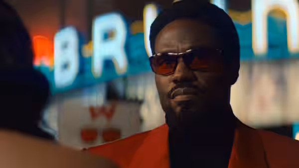 Simon Williams (Yahya Abdul-Mateen II) standing before glowing neon signs at night