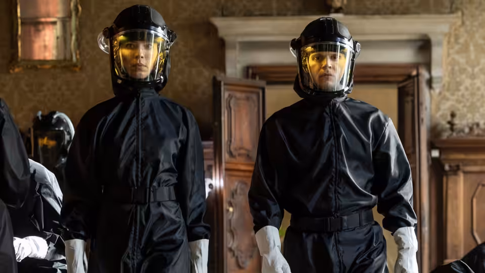 two figures in black hazmat suits standing in a wooden interior