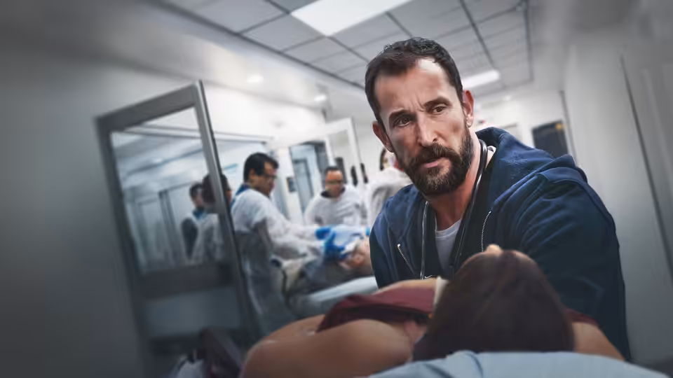 Dr. Robby (Noah Wyle) leans over a patient in the hospital hallway