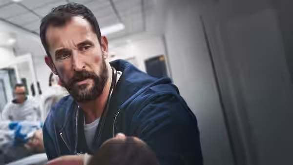Dr. Robby (Noah Wyle) leans forward in a hospital corridor