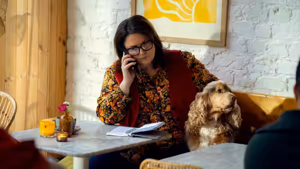 Woman talks on phone at a cafe table with a dog beside her