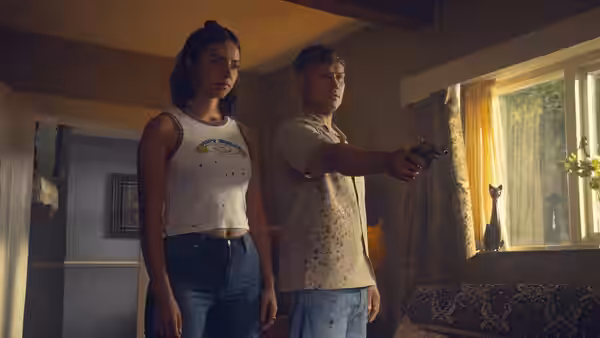 Woman watches as man points handgun out of a living room window