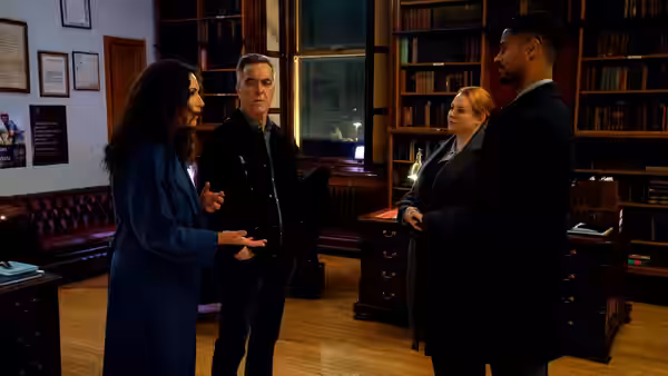Four people converse in an office with bookshelves and leather furniture