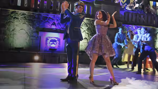 Ben (Mitchell Hope) claps as Audrey dances on a stage with a crowd behind them
