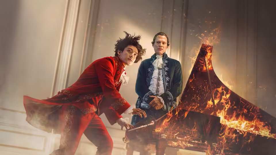 Mozart (Will Sharpe) reaches toward a flaming piano as Salieri (Paul Bettany) watches