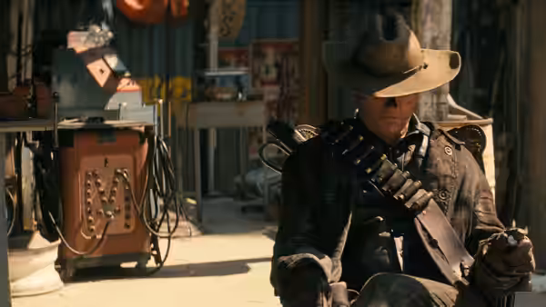 The Ghoul (Walton Goggins) sits in a workshop wearing a cowboy hat