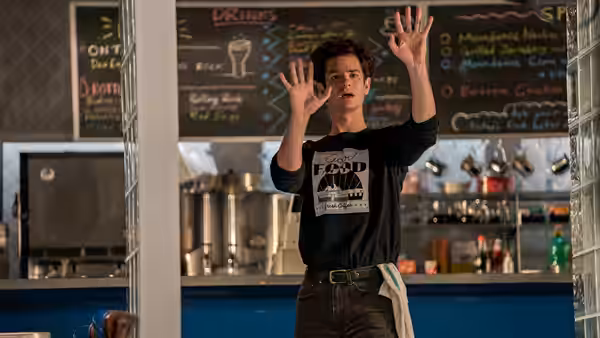 Jonathan Larson (Andrew Garfield) raising both hands in a busy kitchen