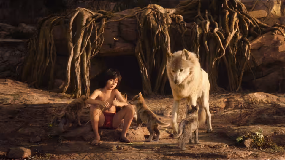 Mowgli (Neel Sethi) sits among wolves outside a root-covered den