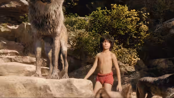 Mowgli (Neel Sethi) stands on rocks beside a tall wolf