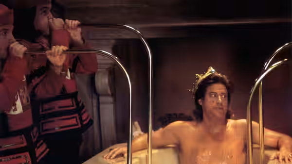 Prince John (Richard Lewis) sits in a tub wearing a crown while guards watch