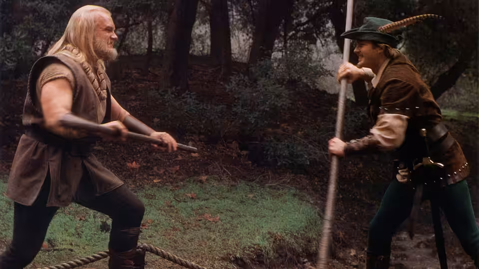 Little John (Eric Allan Kramer) and Robin Hood (Cary Elwes) clash with staffs in the forest