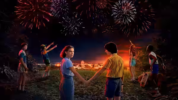 children holding hands in a field while watching fireworks overhead