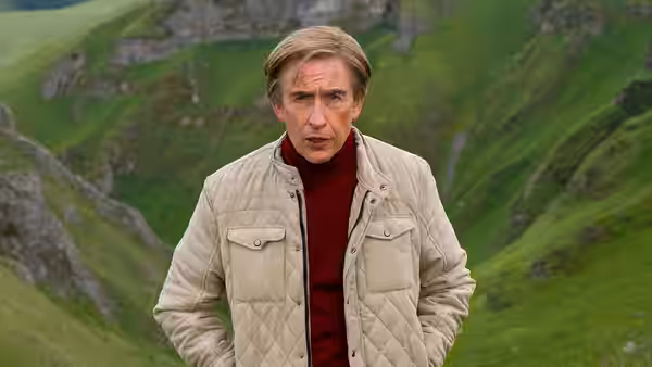 Alan Partridge (Steve Coogan) standing on a green hillside