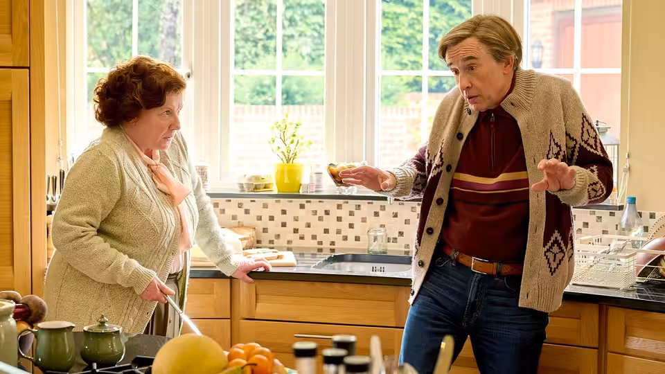 Alan Partridge (Steve Coogan) gesturing in kitchen with Lynn (Felicity Montagu)