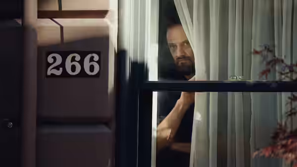 A bearded man looking out a window beside house number 266