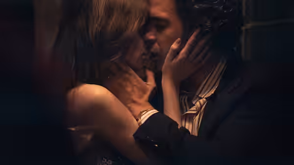 A man and a woman embrace and kiss in a dimly lit room