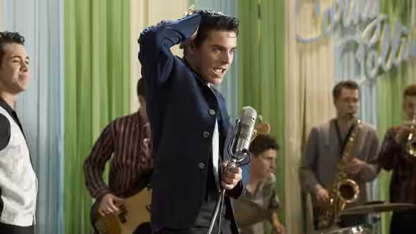 Corny Collins (James Marsden) singing into a microphone on stage