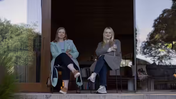 Marissa Irvine (Sarah Snook) and Jenny Kaminski (Dakota Fanning) seated outside a house holding drinks