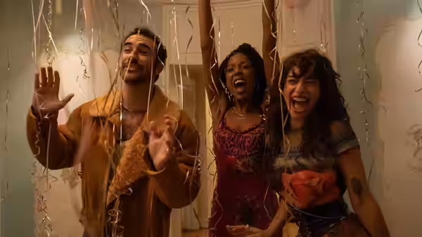 Three people laugh and gesture amid falling streamers in a room