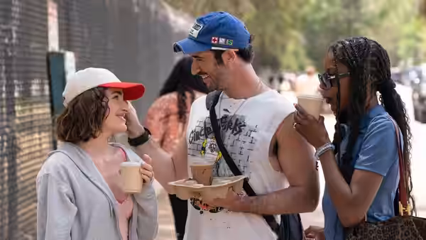 Three young adults stand together holding coffee cups outdoors