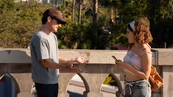 A man gestures while speaking to a woman on a concrete bridge