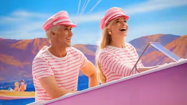 Ken and Barbie smiling while riding in a pink convertible by the sea