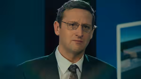 Ron Trosper (Tim Robinson) in a suit and tie in an office