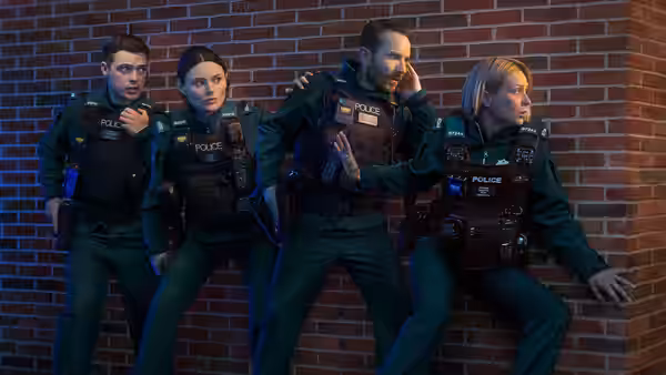 Four police officers in green uniforms leaning against a brick wall at night