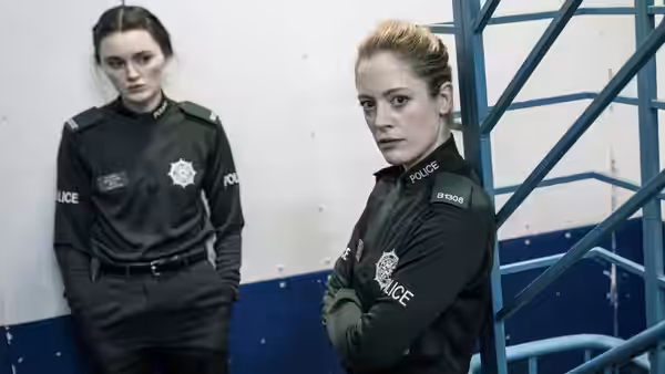 Two female police officers standing indoors near a blue staircase
