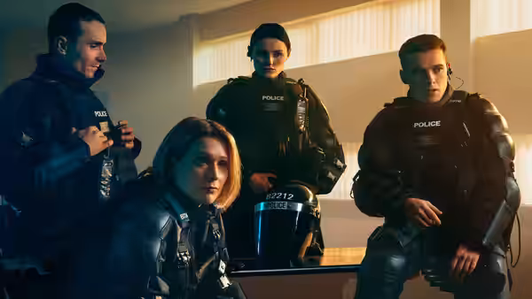 Four police officers in black tactical gear posing together indoors near a window