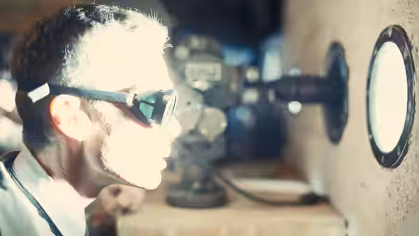 A man in goggles peers through a small window at laboratory equipment