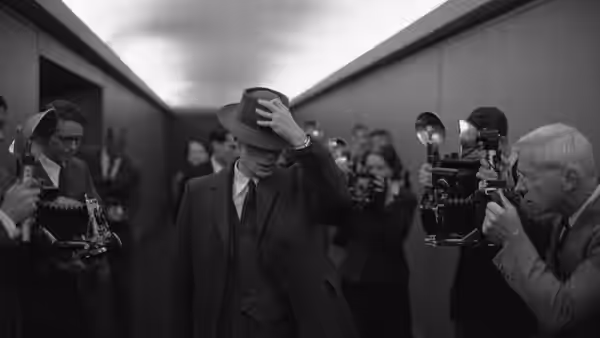 J. Robert Oppenheimer (Cillian Murphy) adjusting his hat as photographers gather in a corridor