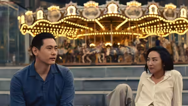 Hae Sung (Teo Yoo) and Nora (Greta Lee) sitting before a lit carousel