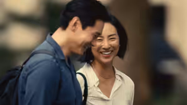 Hae Sung (Teo Yoo) and Nora (Greta Lee) smiling closely together outdoors