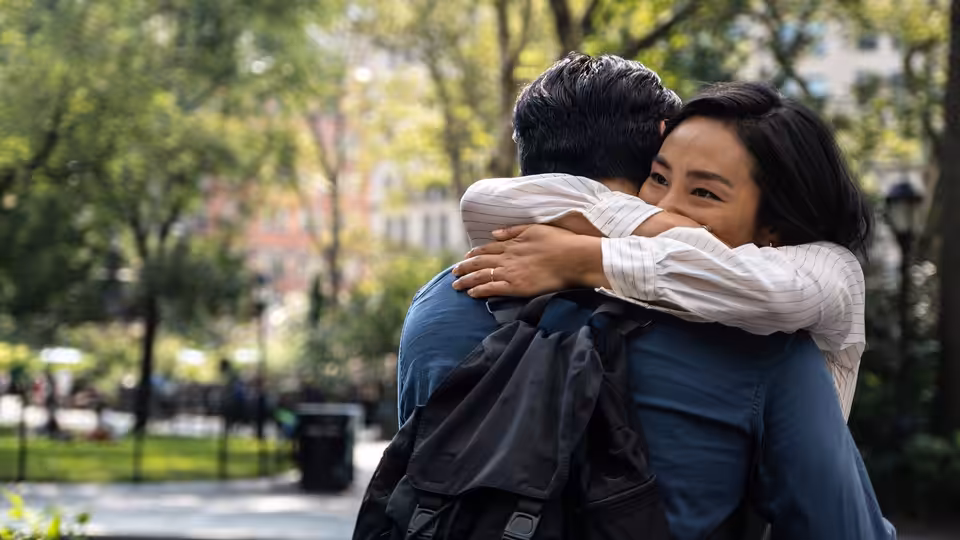 Nora (Greta Lee) hugging Hae Sung (Teo Yoo) from behind in a park