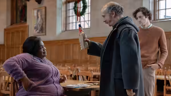 Paul Hunham holding a bottle while speaking to Mary Lamb in a dining hall