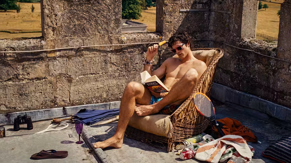 Felix Catton (Jacob Elordi) reading a book in a wicker chair at ruins